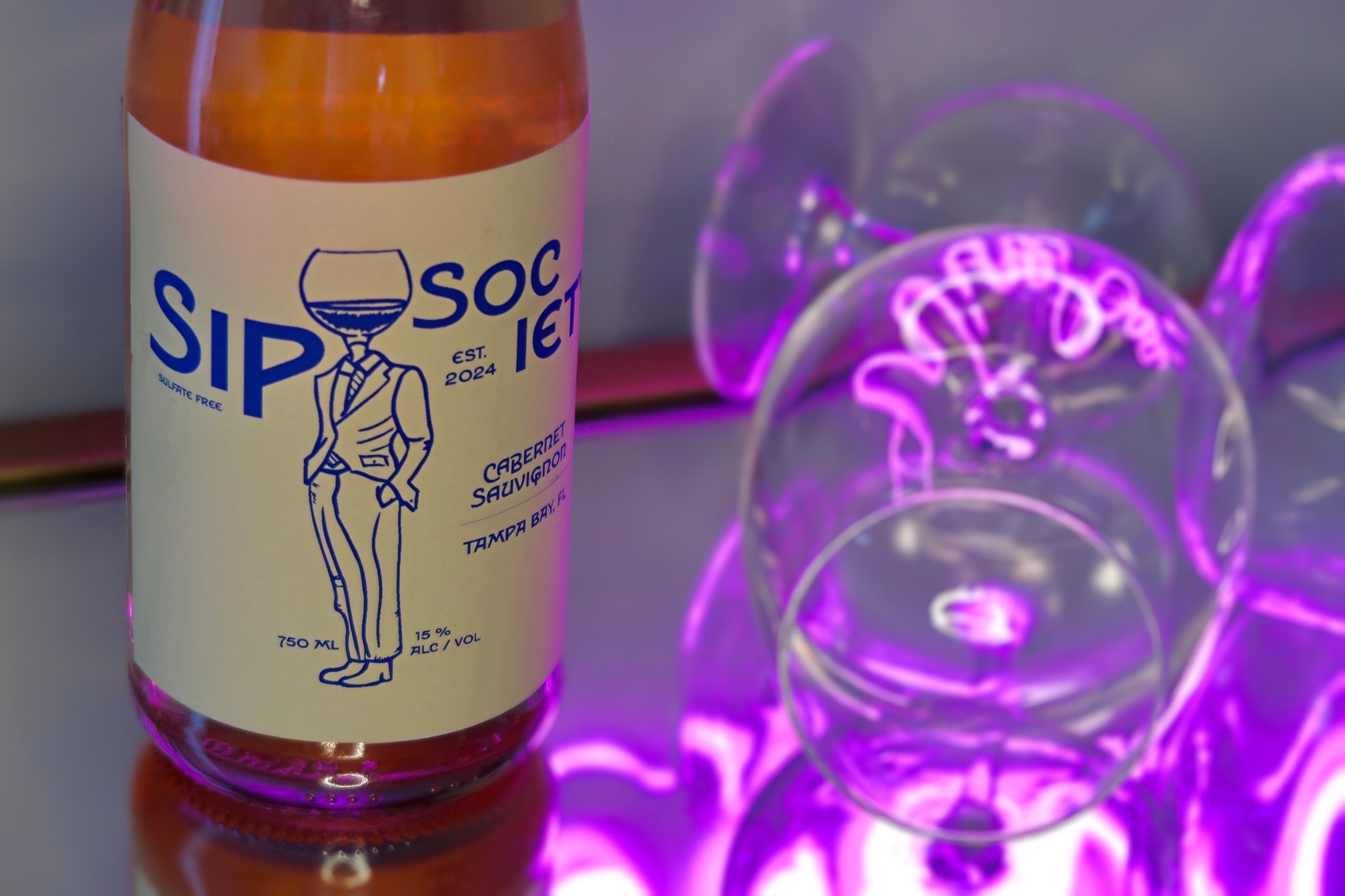 Sip Society wine bottle packaging photographed with glassware and neon light