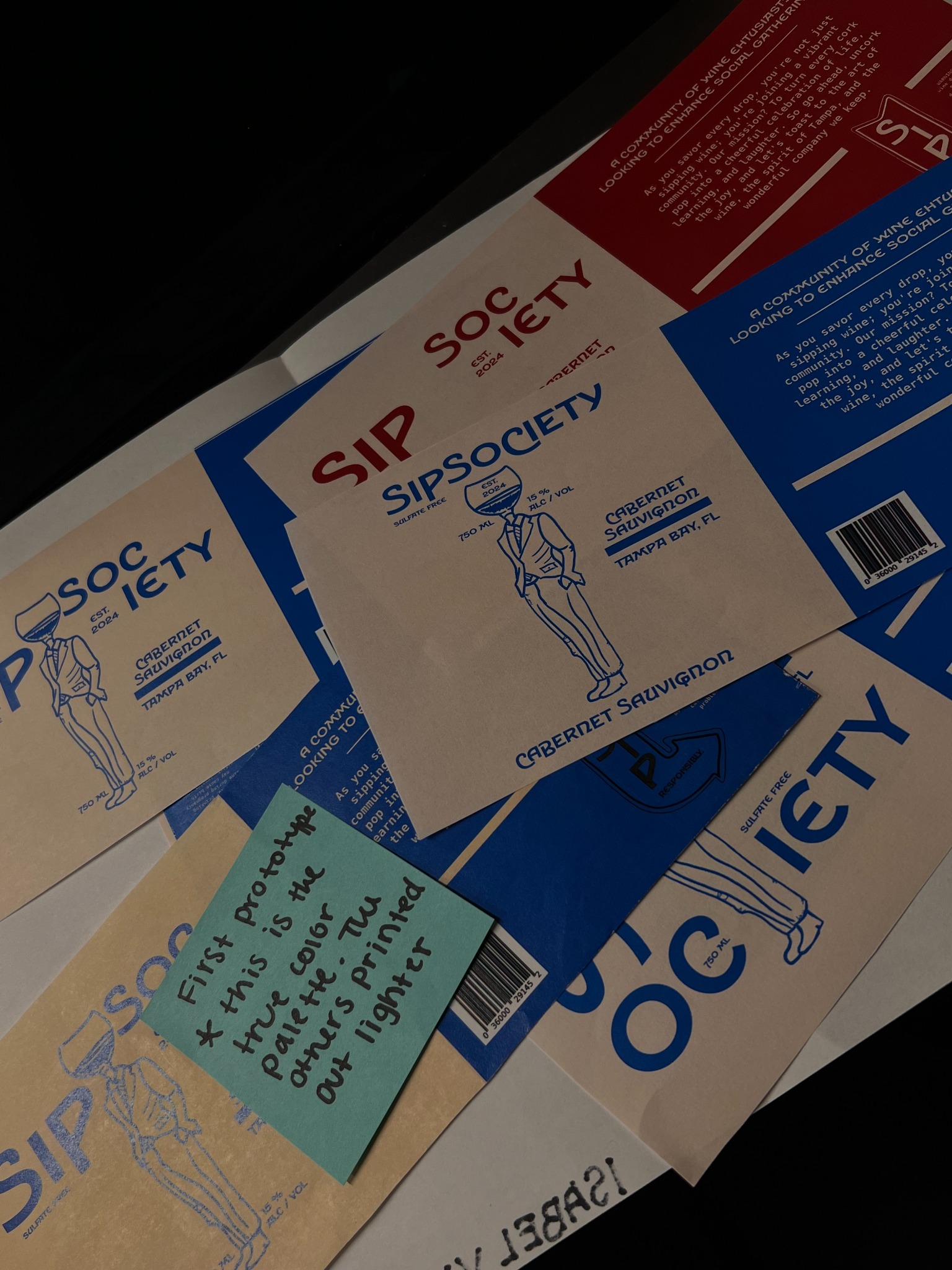 Printed Sip Society label iterations showing cream, blue, and red color testing.